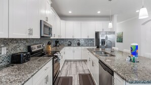 A modern kitchen with white cabinets, granite countertops, a stainless steel refrigerator, and a microwave. - Kissimmee Retreat  6BR House Sleeps 14 (Kissimmee)