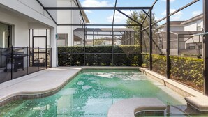 A swimming pool with a glass enclosure, surrounded by a white building and a hedge. - Kissimmee Retreat  6BR House Sleeps 14 (Kissimmee)