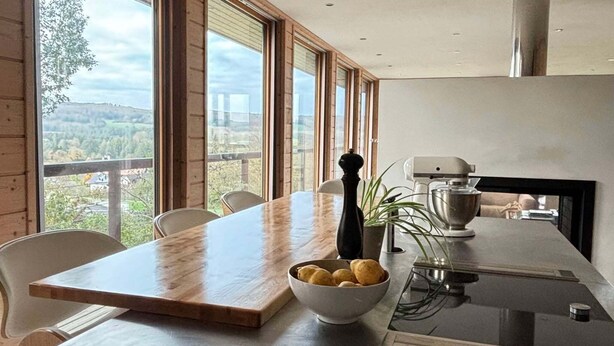 Eine moderne Küche mit einer großen Kochinsel, Holzböden und großen Fenstern mit Blick ins Freie.