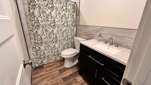 A bathroom with a shower curtain, toilet, sink, and wooden flooring.