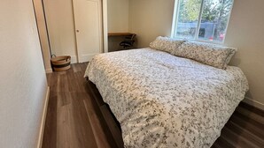 A bedroom with a bed, a window, a closet, and a small table.