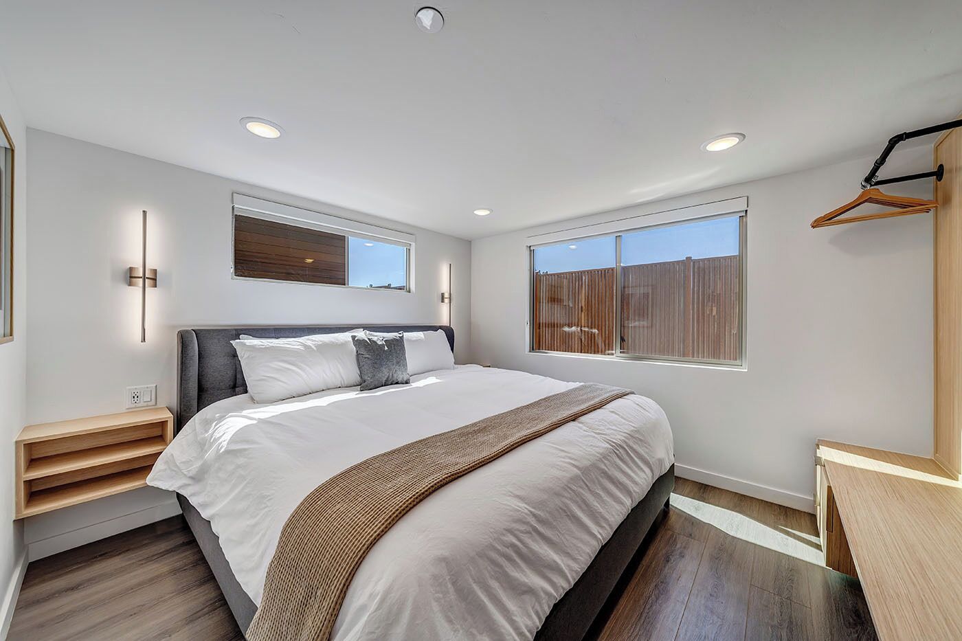 Un dormitorio moderno con una cama grande, mesitas de noche, una ventana y un banco de madera.