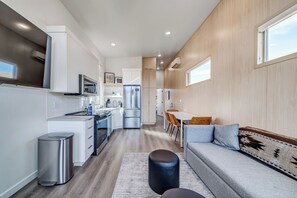 A modern kitchen with white cabinets, stainless steel appliances, and a dining area with a grey sofa and wooden chairs.