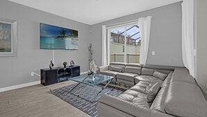 A modern living room with a sectional sofa, a glass coffee table, and a painting of a beach scene.