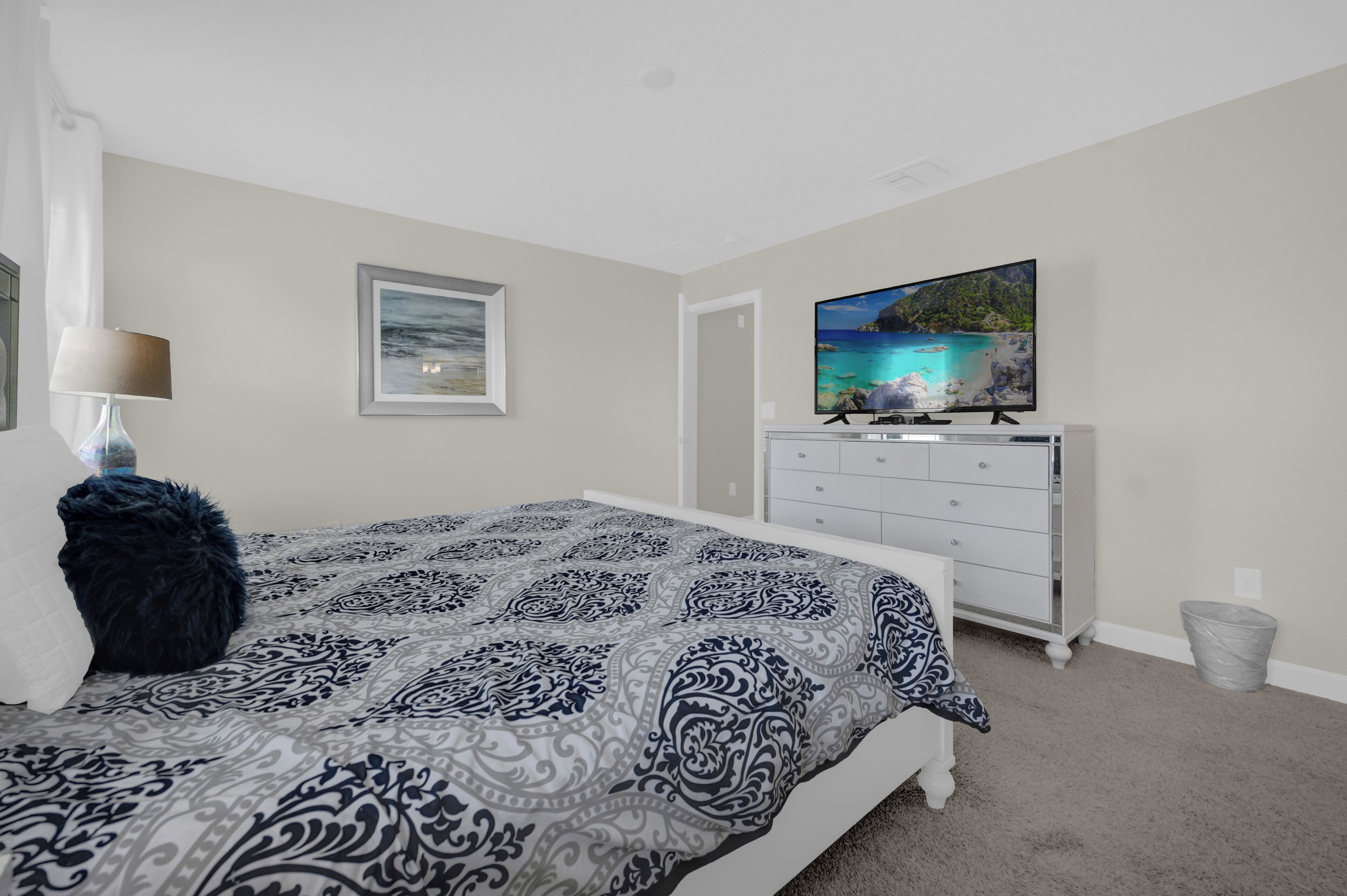 Un dormitorio con cama, cómoda, televisor y un cuadro en la pared.