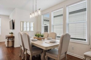Comedor con una mesa preparada para cuatro personas, sillas alrededor y un candelabro sobre ella, además de amplias ventanas con persianas.