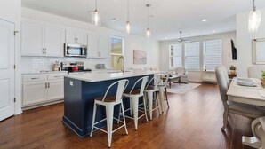 A modern kitchen with white cabinets, a central island with bar stools, and pendant lighting. - 4BR home with  workspace & parking (Oxford)