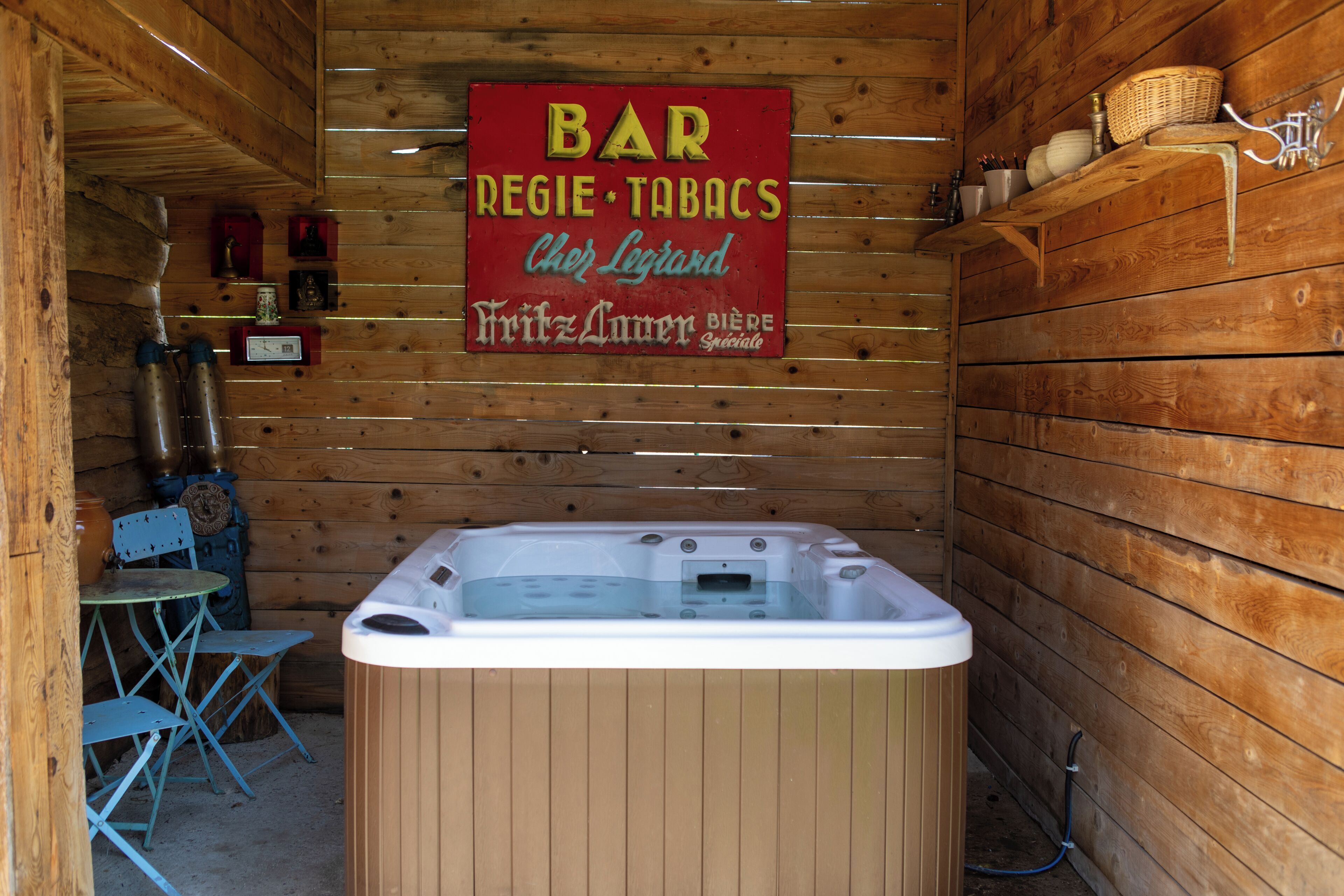 Un intérieur en bois avec un jacuzzi, un panneau indiquant la présence d’un bar et une petite table avec des chaises.