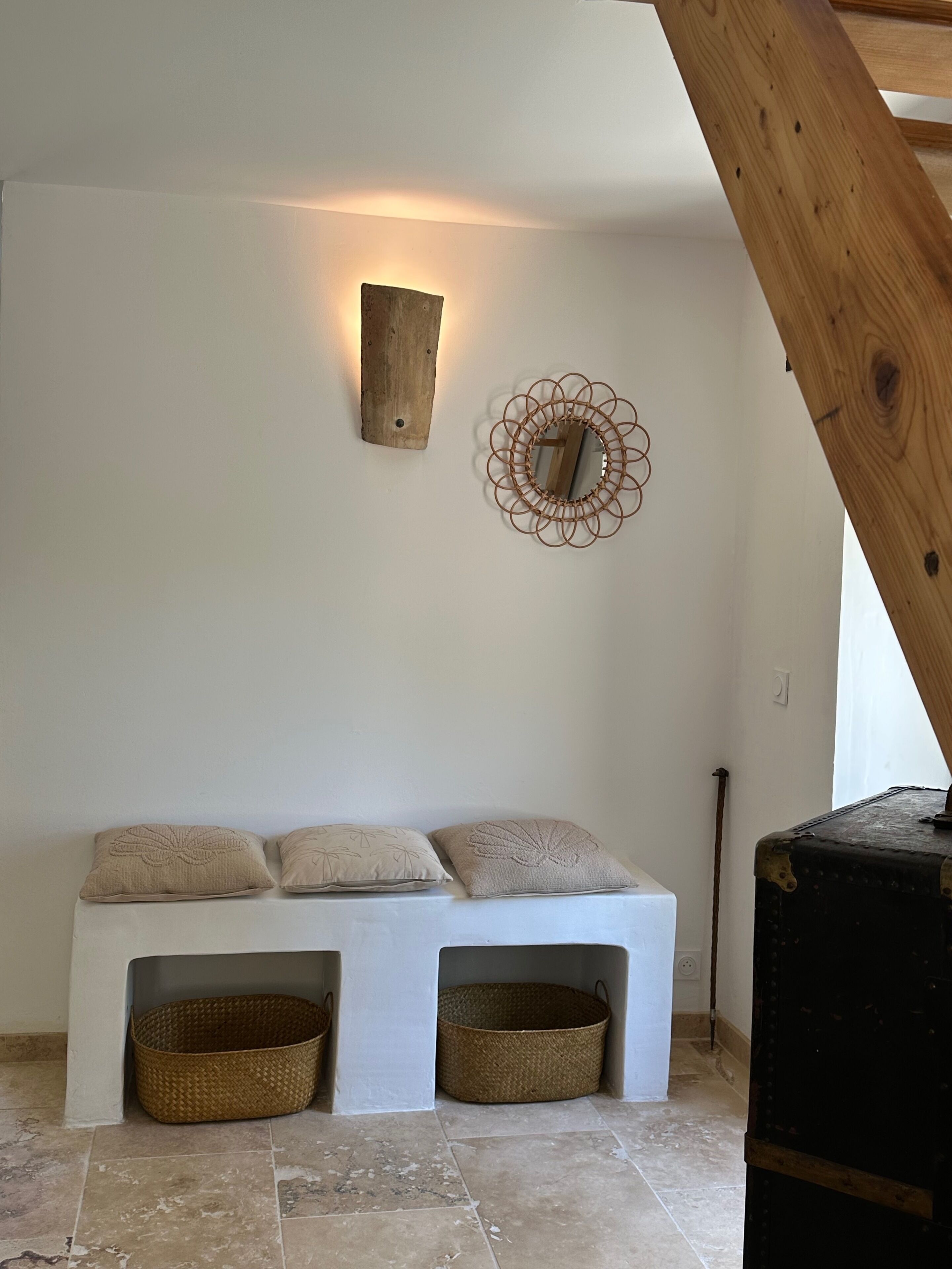 Ein Zimmer mit einer weißen Bank, zwei gewebten Körben, einer Holzdeko und einem Wandspiegel.