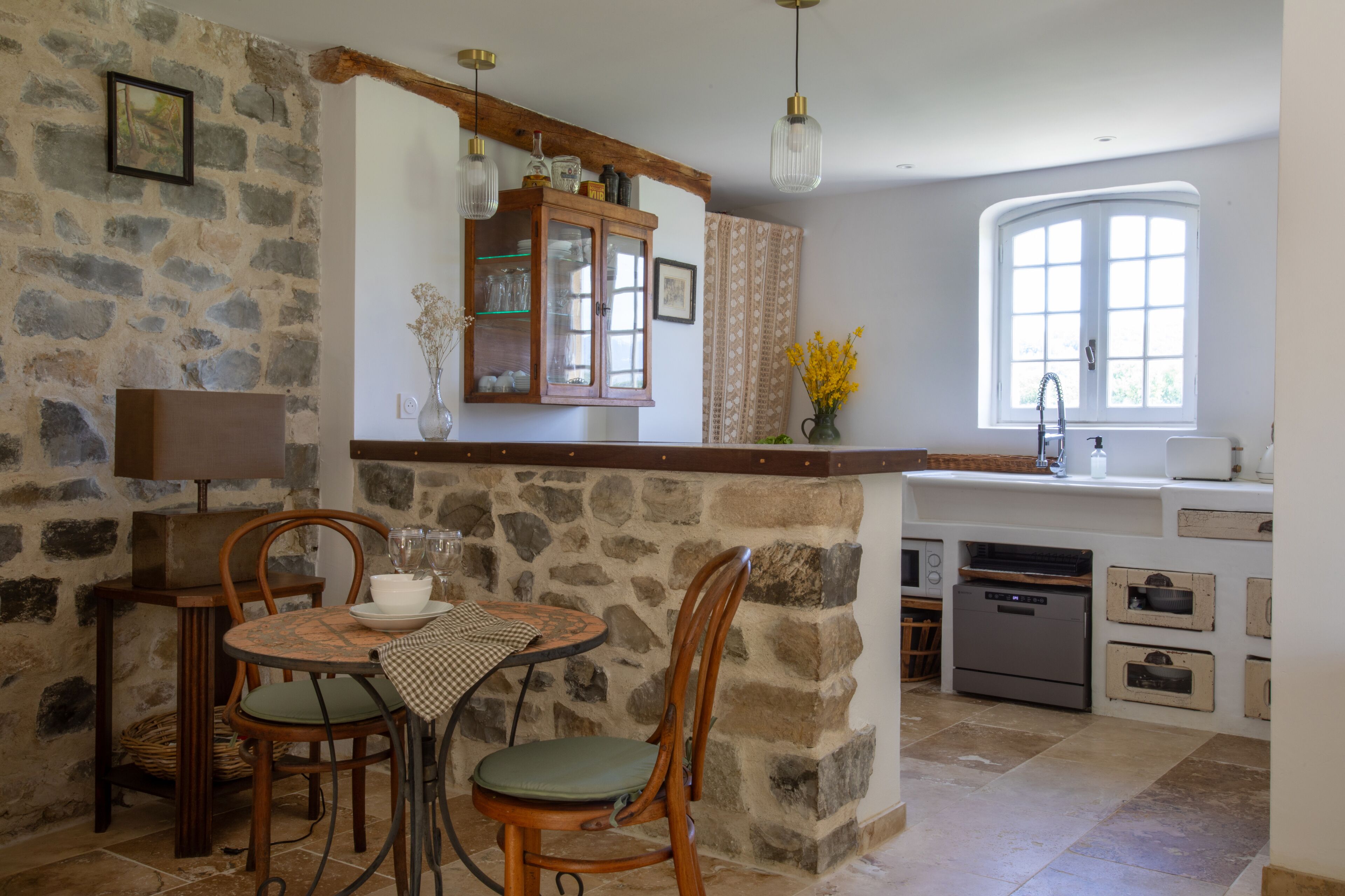 Une cuisine aux murs en pierre, avec des meubles en bois, une table à manger entourée de chaises et une fenêtre offrant une vue agréable.