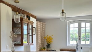 Eine Küche mit einer Steineninsel, Holzstühlen, einem Esstisch und einem Fenster mit Blick ins Grüne.