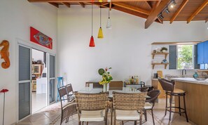 A modern kitchen with a dining area, featuring a glass table, wicker chairs, and pendant lights. - 4BR Home w/ BBQ 100m From Beach Jat0355 (Bombinhas)