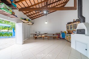 A spacious room with a high ceiling, a wooden bench, a bicycle, and a kitchen area with a stove. - 4BR Home w/ BBQ 100m From Beach Jat0355 (Bombinhas)