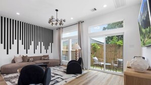 A modern living room with a sofa, chairs, a patterned rug, and a large window with a view of the outdoors. - City Stay Couples, Creators, and Cozy Hub in HTX (Houston)
