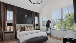 A modern bedroom with a large bed, bedside tables, a mirror, and a view of greenery outside. - City Stay Couples, Creators, and Cozy Hub in HTX (Houston)