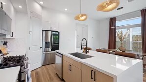 A modern kitchen with white cabinetry, stainless steel appliances, a central island with a sink, and pendant lighting. - Luxury 3BR Houston - Near Downtown & Stadiums (Houston)