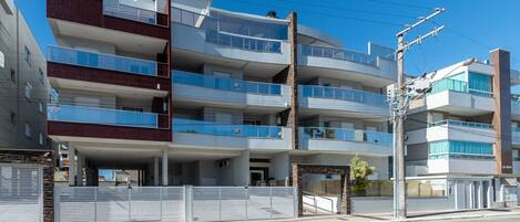 A multi-story residential building with balconies, a gated entrance, and a clear blue sky.