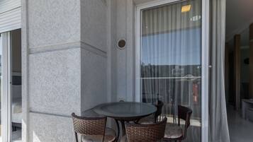 En balkon med glasdør, et rundt bord og fire fletstole.