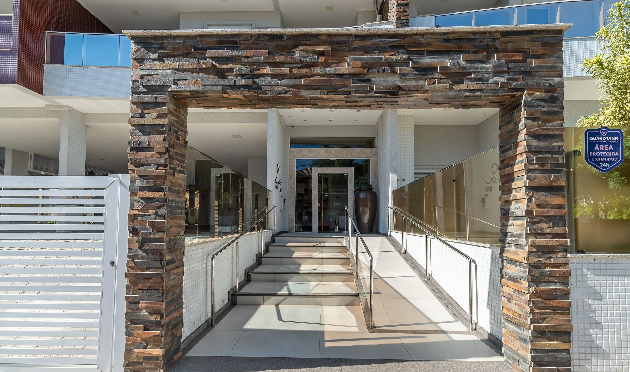 Una entrada moderna a un edificio, con un arco de piedra, puertas de cristal y una barandilla metálica.