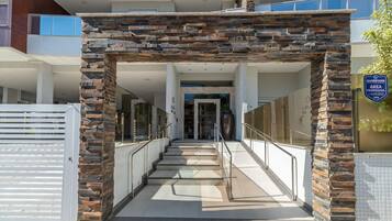 Una entrada moderna a un edificio, con un arco de piedra, puertas de cristal y una barandilla metálica.