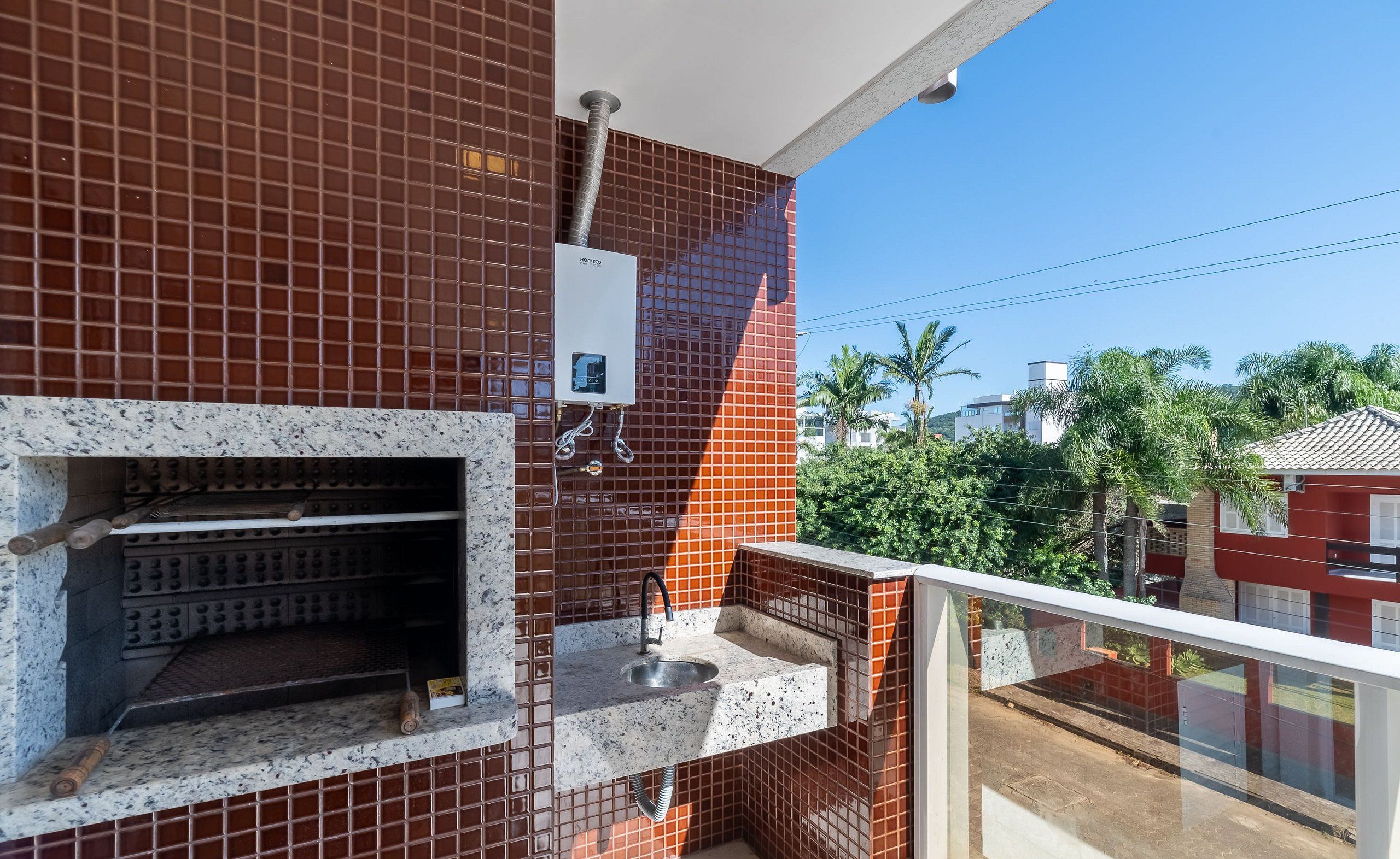 Un balcón con un muro de azulejos, un calentador de agua y un lavamanos pequeño.