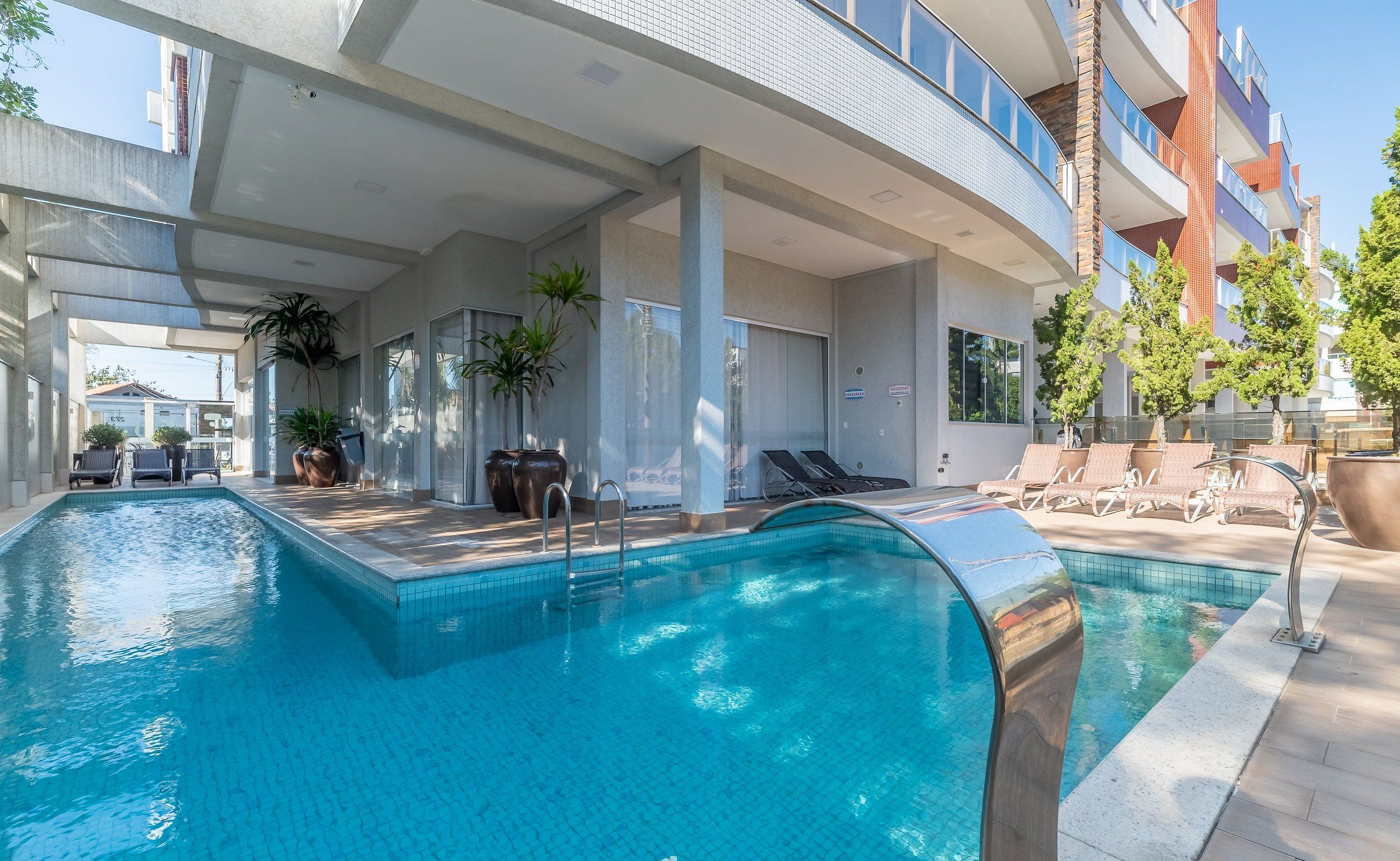 Un hotel moderno con una amplia piscina cubierta, tumbonas y plantas en macetas.