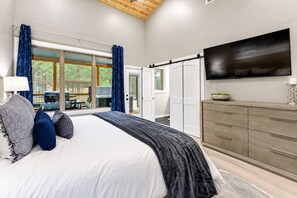 A bedroom with a large bed, a TV mounted on the wall, and a sliding door leading to an outdoor area. - Kids Play Zones | Hot Tub | 3 Arcades | Family Fun (Broken Bow)