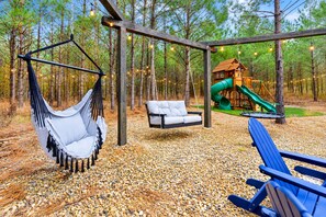 A hammock, a swing, and a slide in a wooded park area. - Kids Play Zones | Hot Tub | 3 Arcades | Family Fun (Broken Bow)
