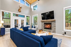 A modern living room with a sectional sofa, a fireplace, and a television. - Kids Play Zones | Hot Tub | 3 Arcades | Family Fun (Broken Bow)