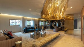 Un salón amplio con sofá, mesa de centro y un banco. Hay un ventanal grande y una estantería con objetos decorativos.
