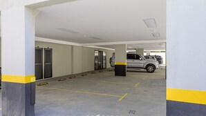 Un parking avec des places de stationnement délimitées, une voiture et l’entrée d’un immeuble.