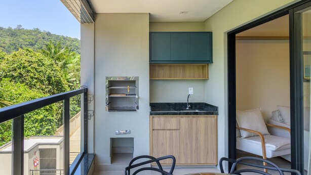 Un balcon avec une table à manger, des chaises, un coin cuisine équipé de placards et d’un évier, et une vue sur une colline verdoyante.