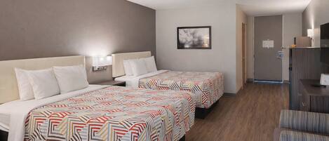 A hotel room with two beds, a desk, a chair, a television, and a door.