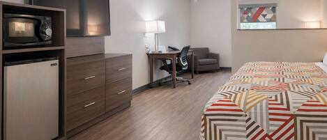 A hotel room with a bed, a desk, a chair, a TV, and a microwave.