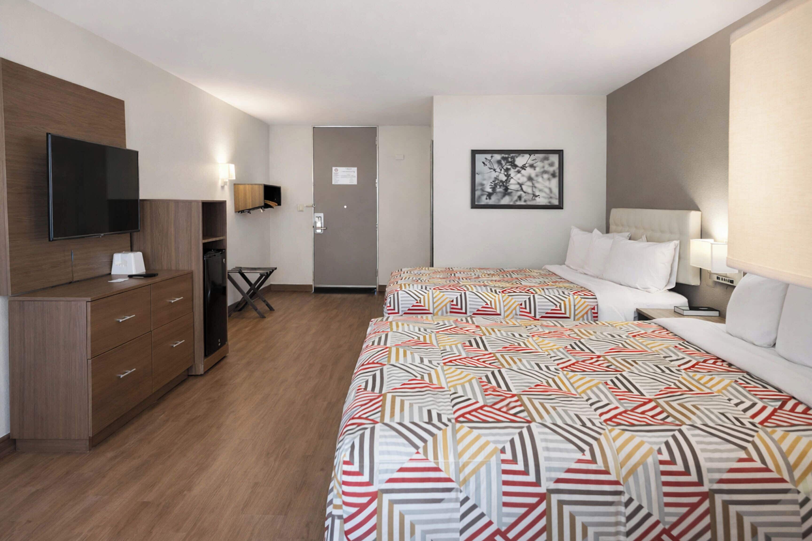 Habitación de hotel con dos camas, televisión, escritorio y armario.