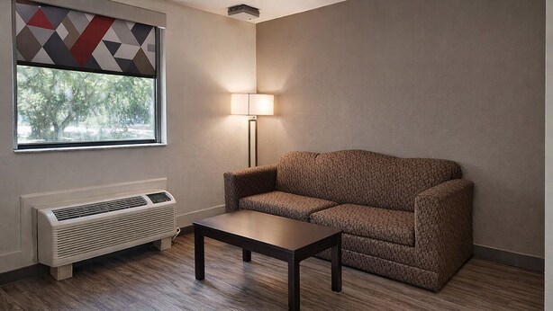 A room with a window, a sofa, a table, and a wall-mounted heater. - Motel 6 – Lake City, Fl – Medical Center (Lake City)