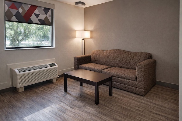 A room with a window, a sofa, a table, and a wall-mounted heater.