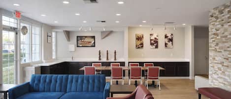 A modern interior with a blue sofa, red chairs, a wooden dining table, and a kitchen area with a white countertop.