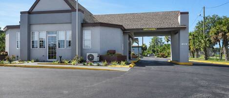 A building with a flat roof, a covered entrance, and a paved parking area.