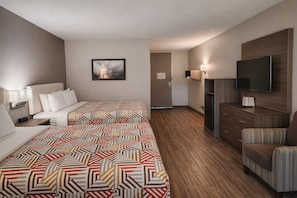 A hotel room with two beds, a TV, a desk, and a chair.