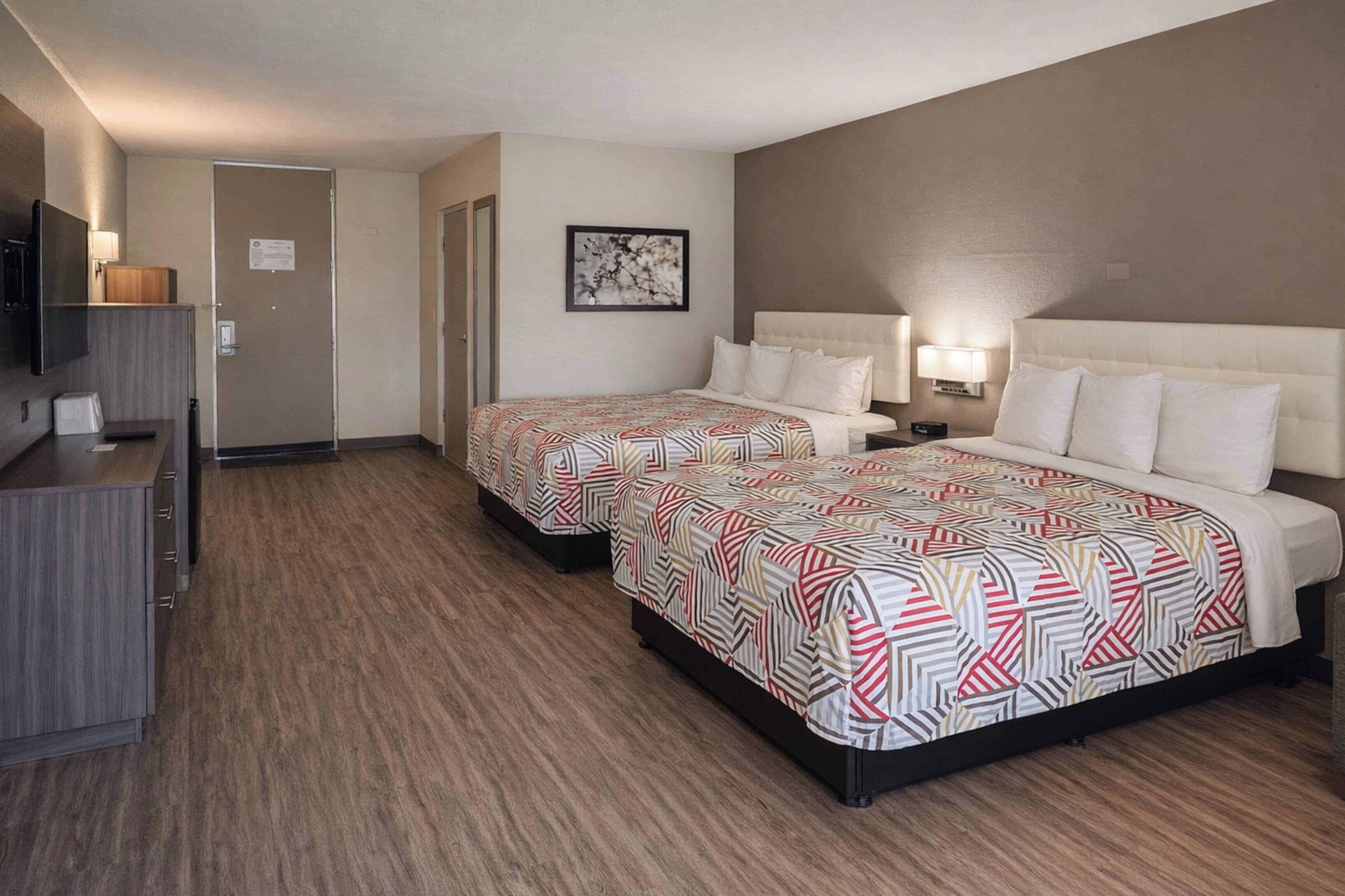 A hotel room with two beds, a desk, a TV, and a door.
