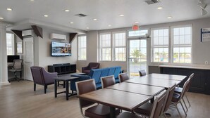 A spacious room with a large table and chairs, a television mounted on the wall, and large windows providing natural light. - Motel 6 – Lake City, Fl – Medical Center (Lake City)