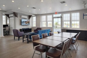 A spacious room with a large table and chairs, a television mounted on the wall, and large windows providing natural light. - Motel 6 – Lake City, Fl – Medical Center (Lake City)