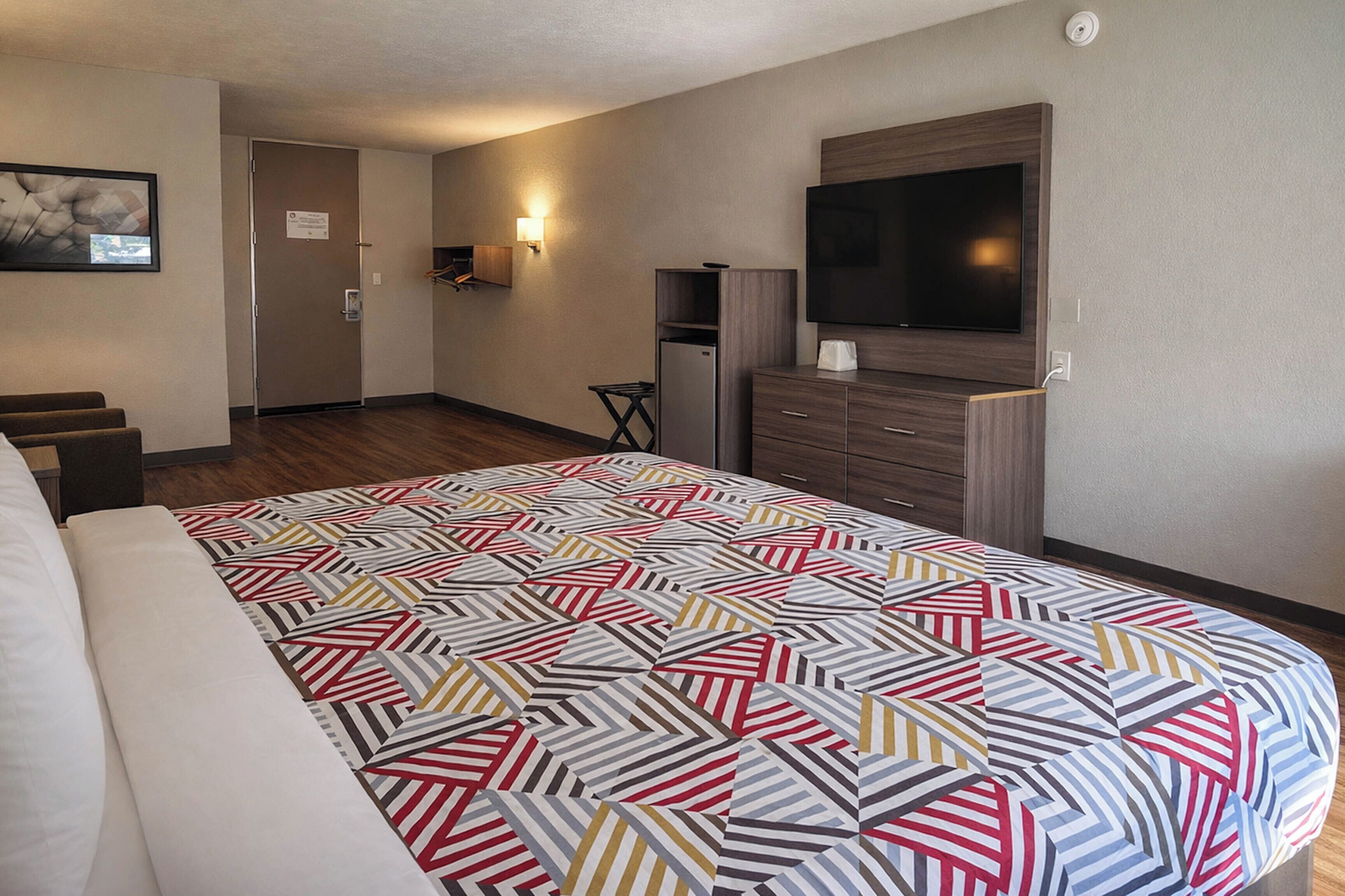 A hotel room with a bed, a TV, a desk, and a refrigerator.