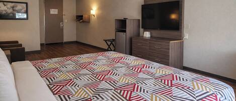 A hotel room with a bed, a TV, a desk, and a refrigerator.