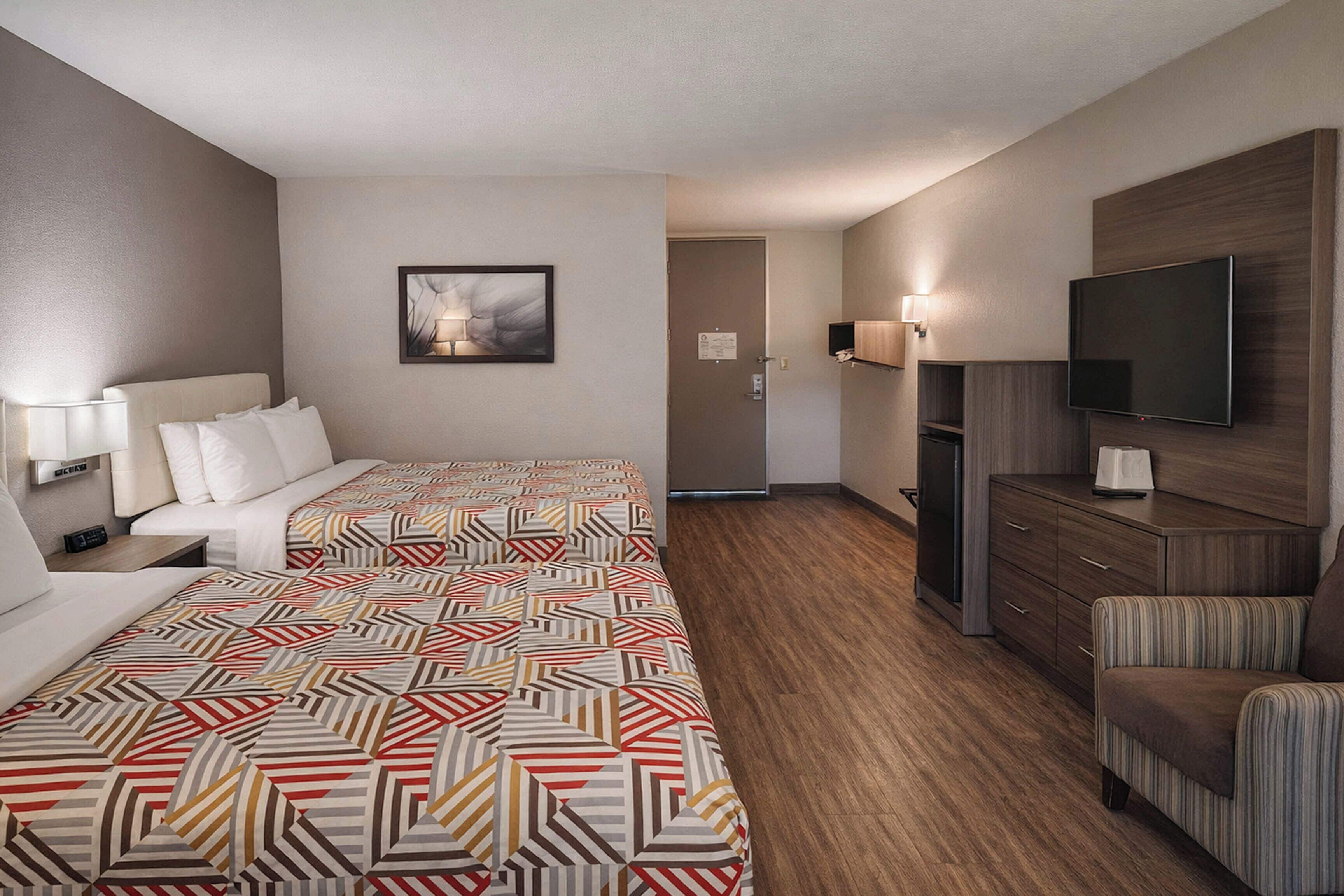 A hotel room with two beds, a TV, a desk, and a chair.