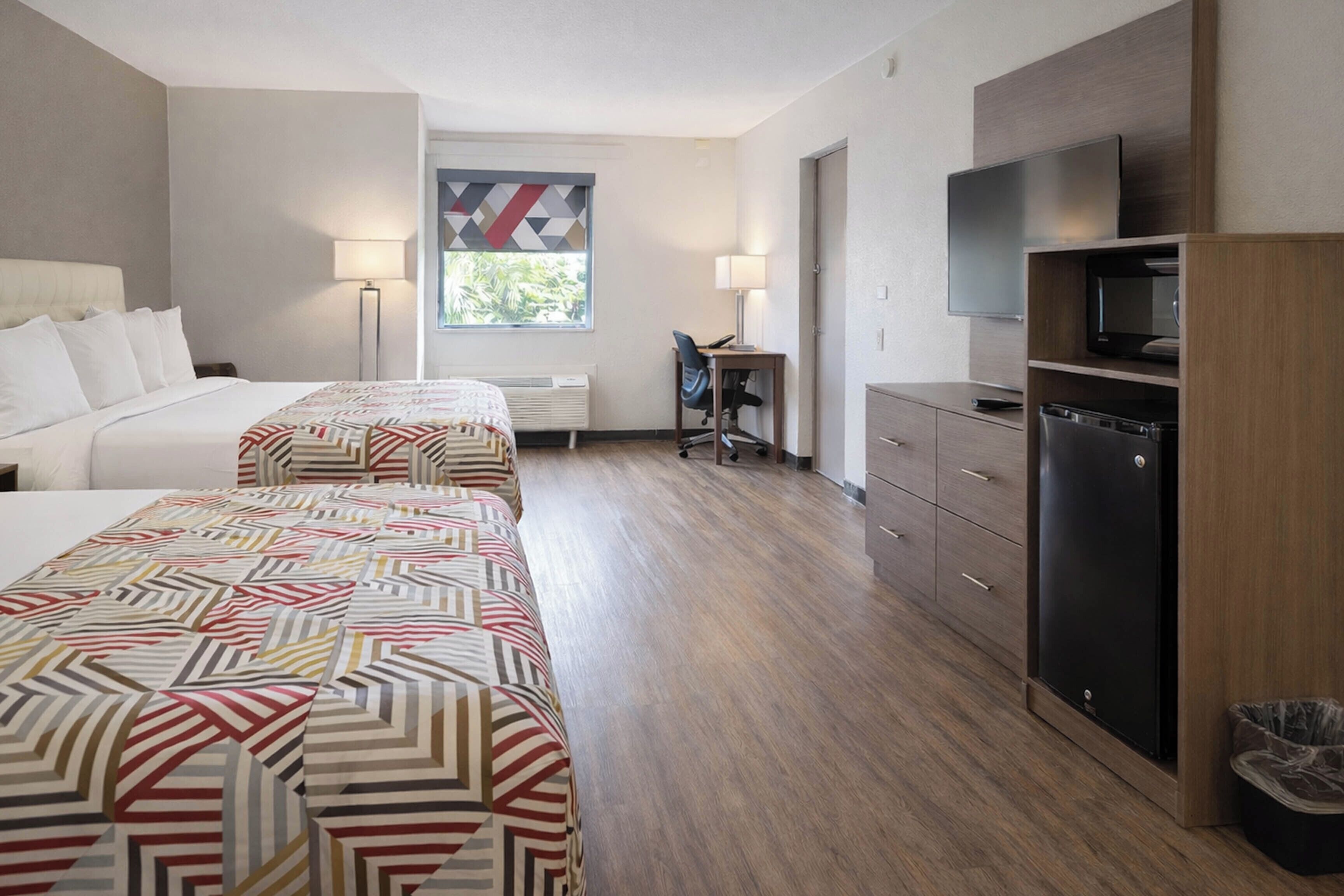 Ein Hotelzimmer mit zwei Betten, einem Schreibtisch, einem Stuhl, einem Fernseher und einem Kühlschrank.