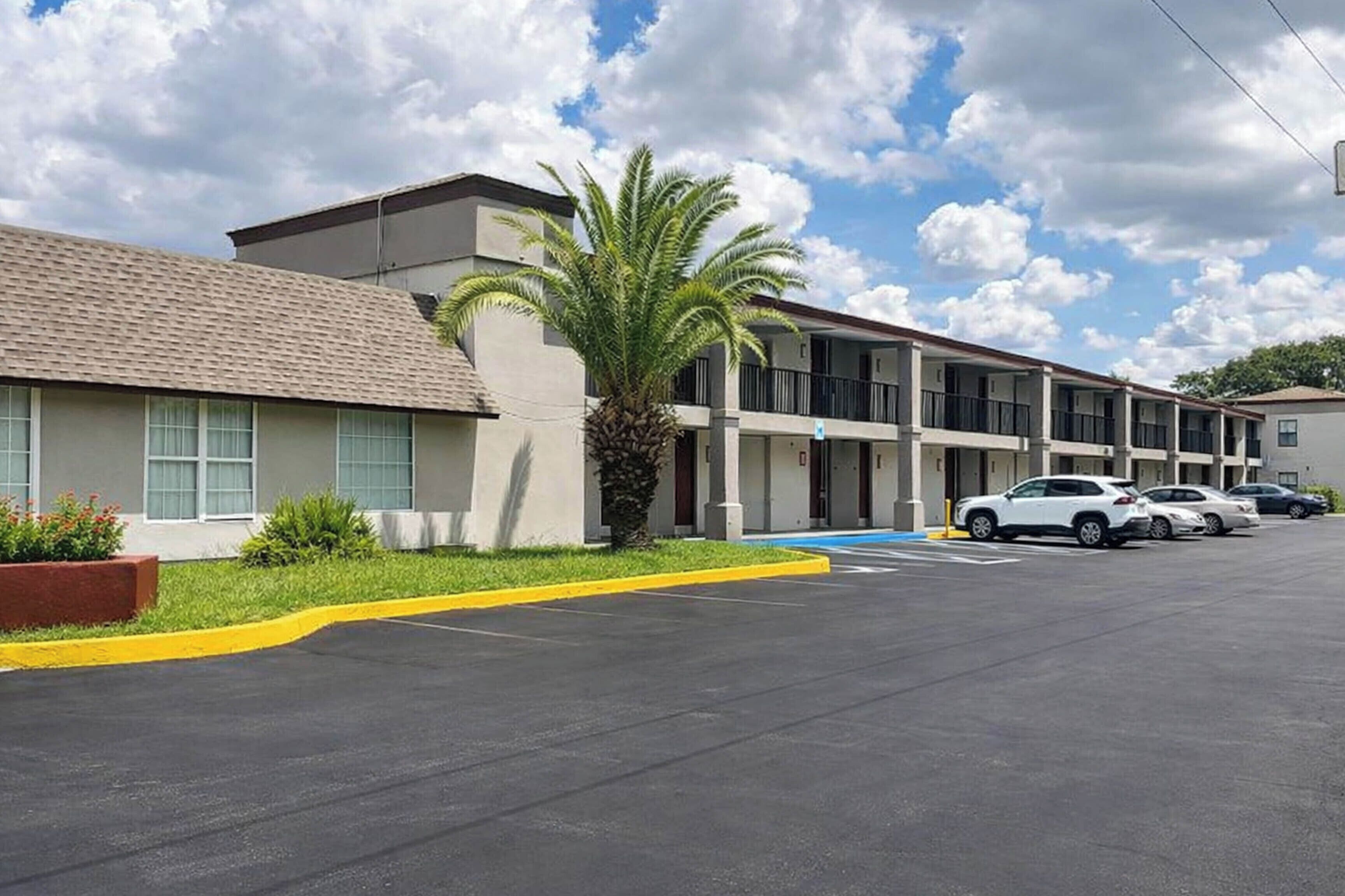 A multi-story motel with a parking lot, a palm tree, and several cars parked.