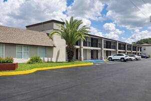Un motel de varios pisos con estacionamiento, una palmera y varios coches aparcados.