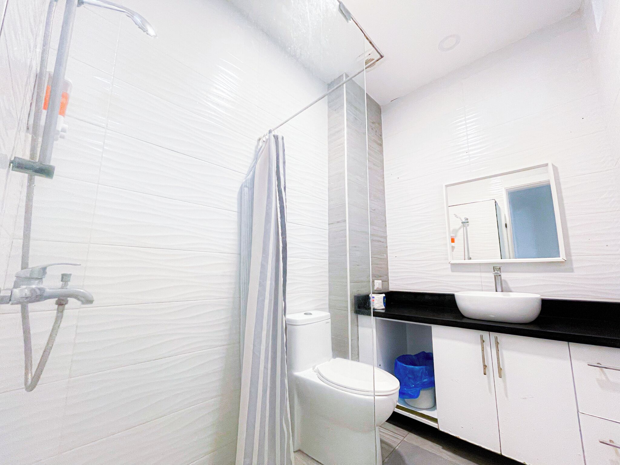 A bathroom with white tiled walls, a shower, a toilet, a sink, and a mirror.